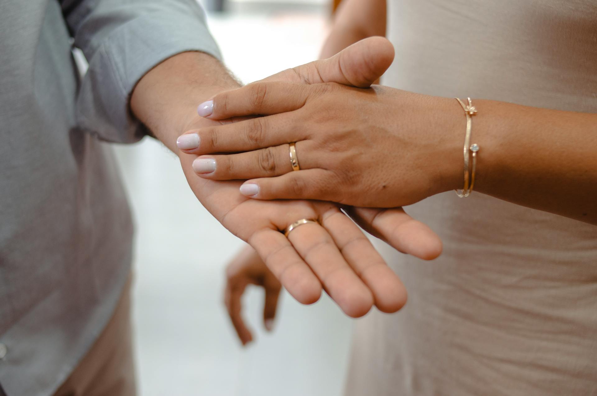 Close-up of a couple holding hands showcasing gold rings and bracelets.