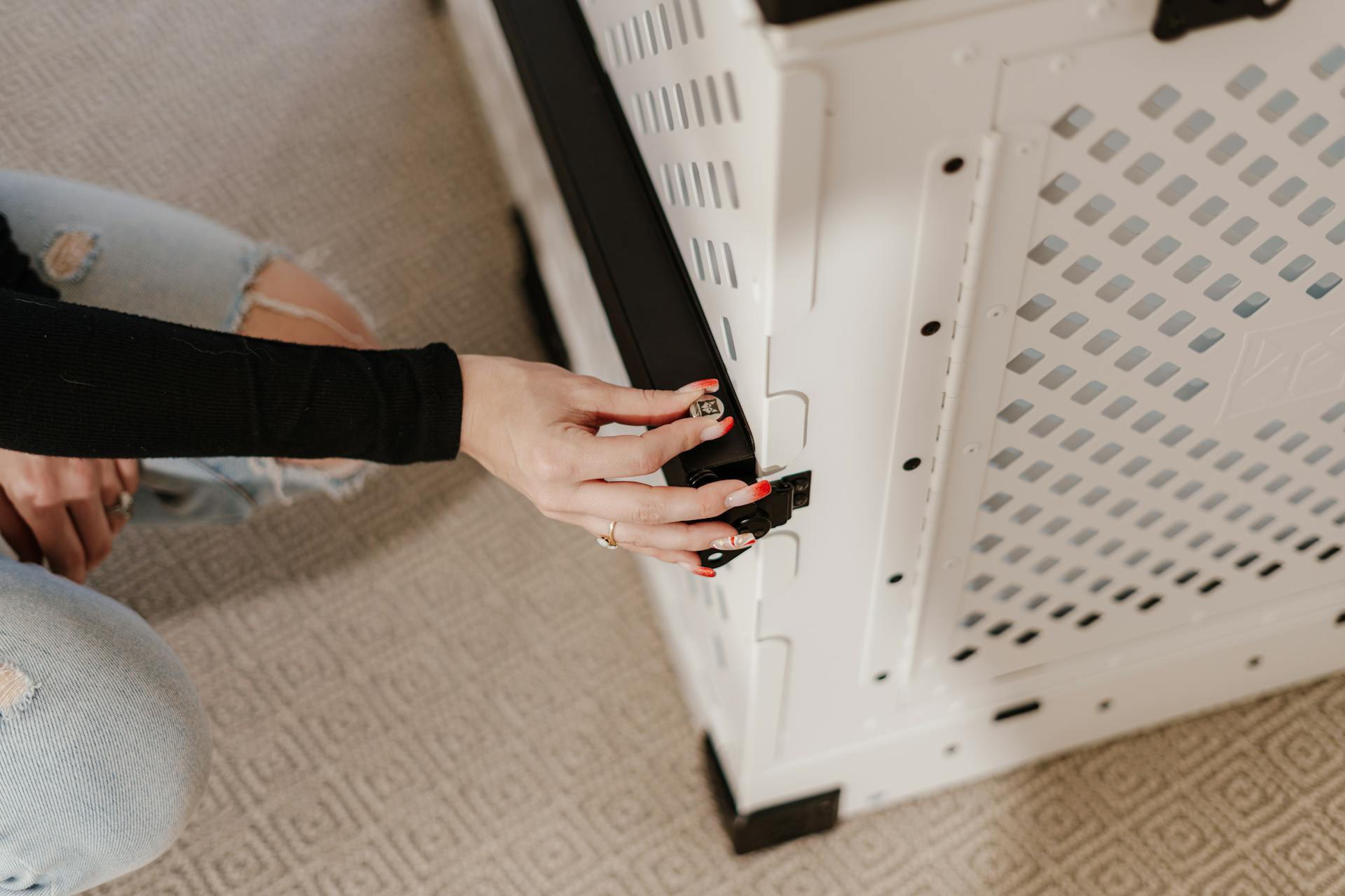 Close-up of a woman securing a high-quality dog crate indoors, showing safety features.