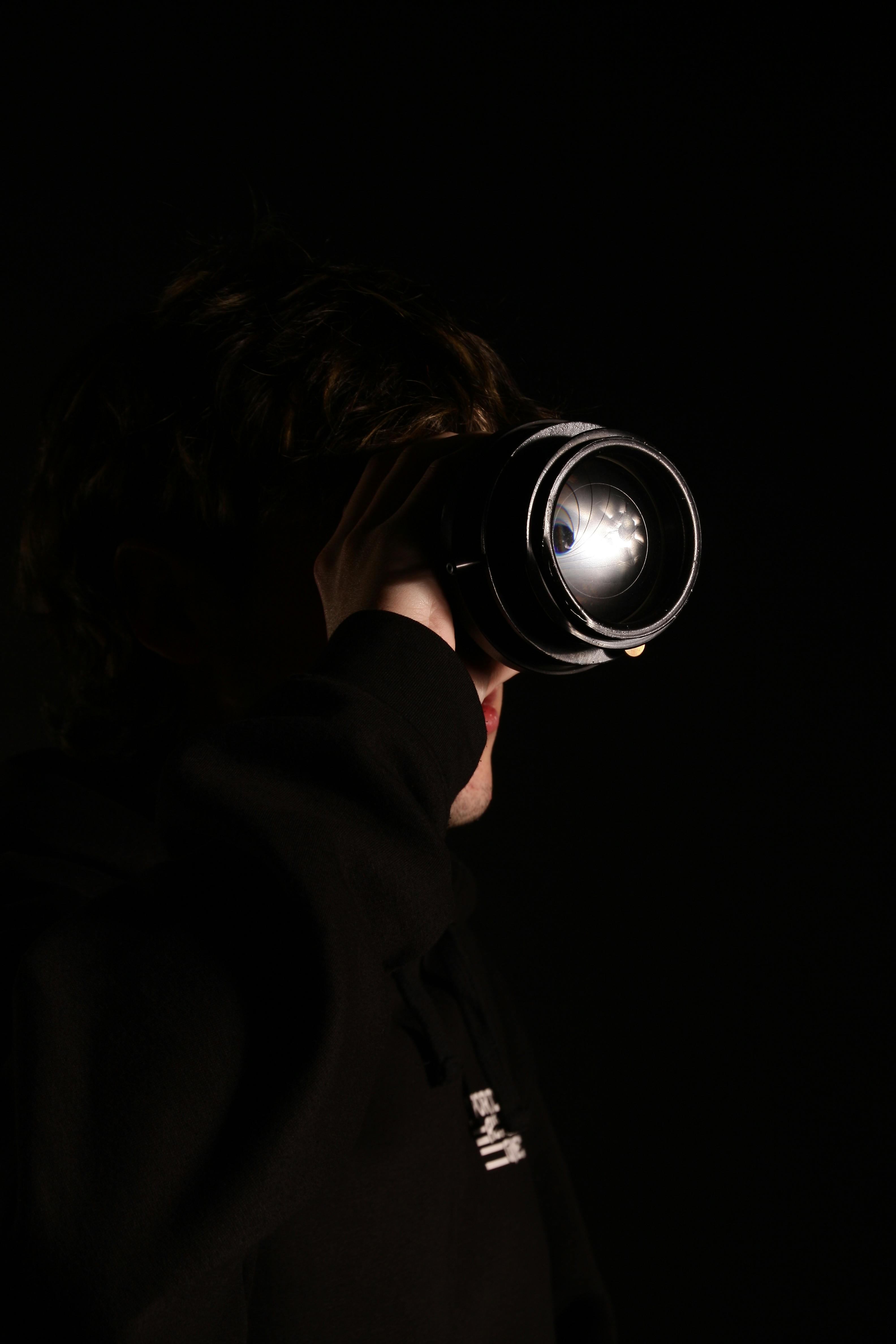 Moody portrait of a man observing through a camera lens, highlighting contrast and shadows.