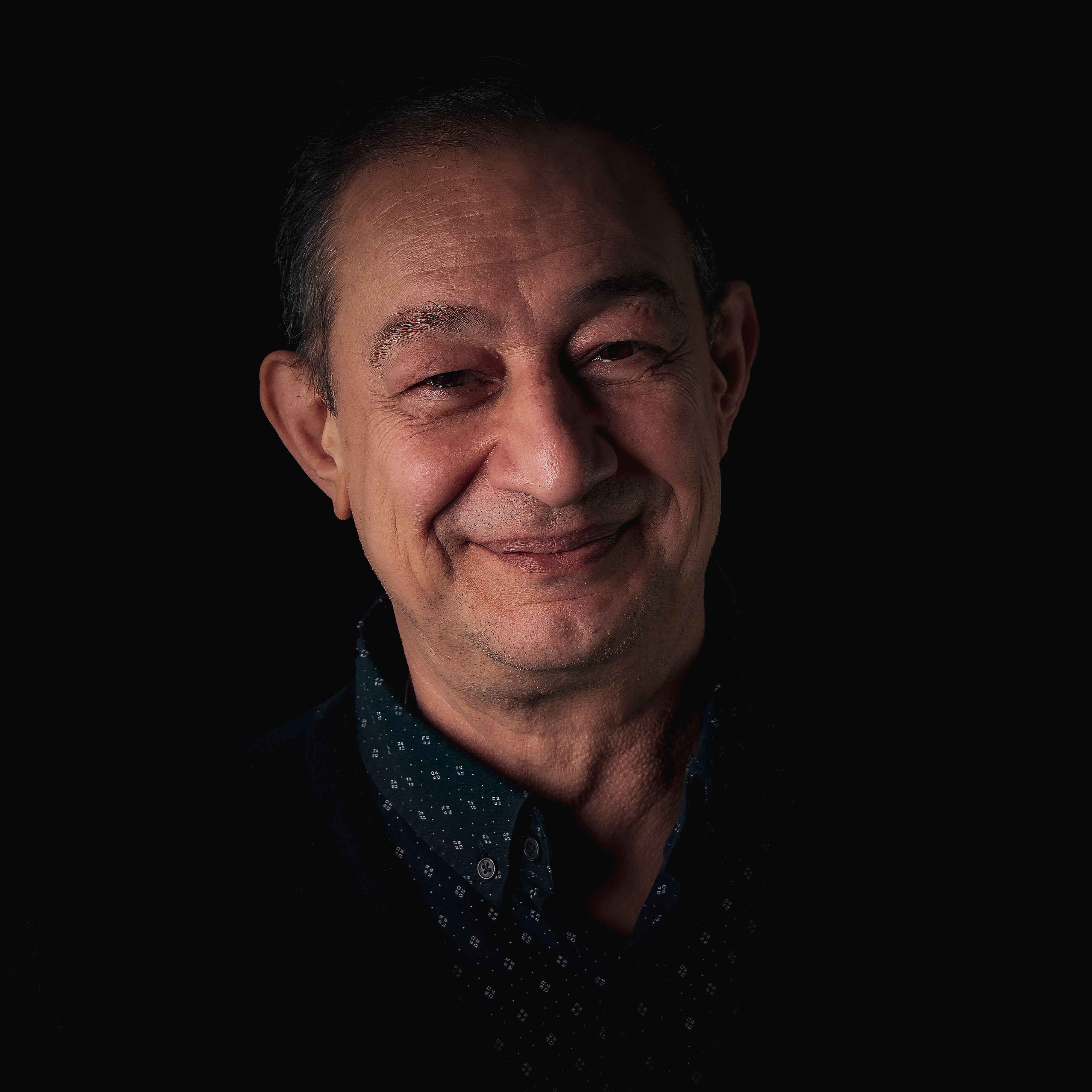 A close-up portrait of a smiling elderly man against a dark background, highlighting his warm expression.