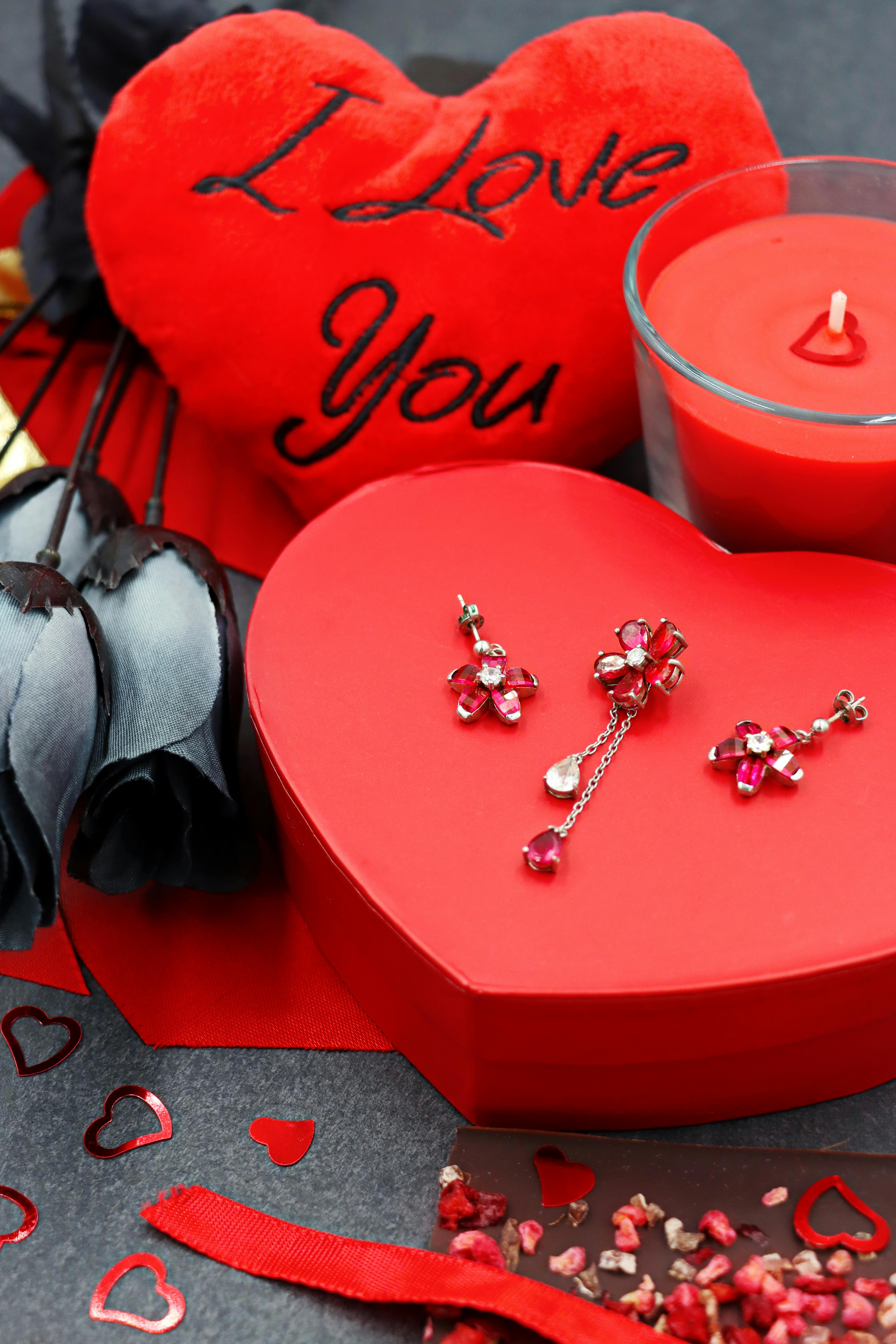 A romantic Valentine's Day setup with a heart pillow, jewelry, candles, and red roses.