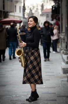 A fashionable woman playing saxophone on a bustling street, captivating passersby.