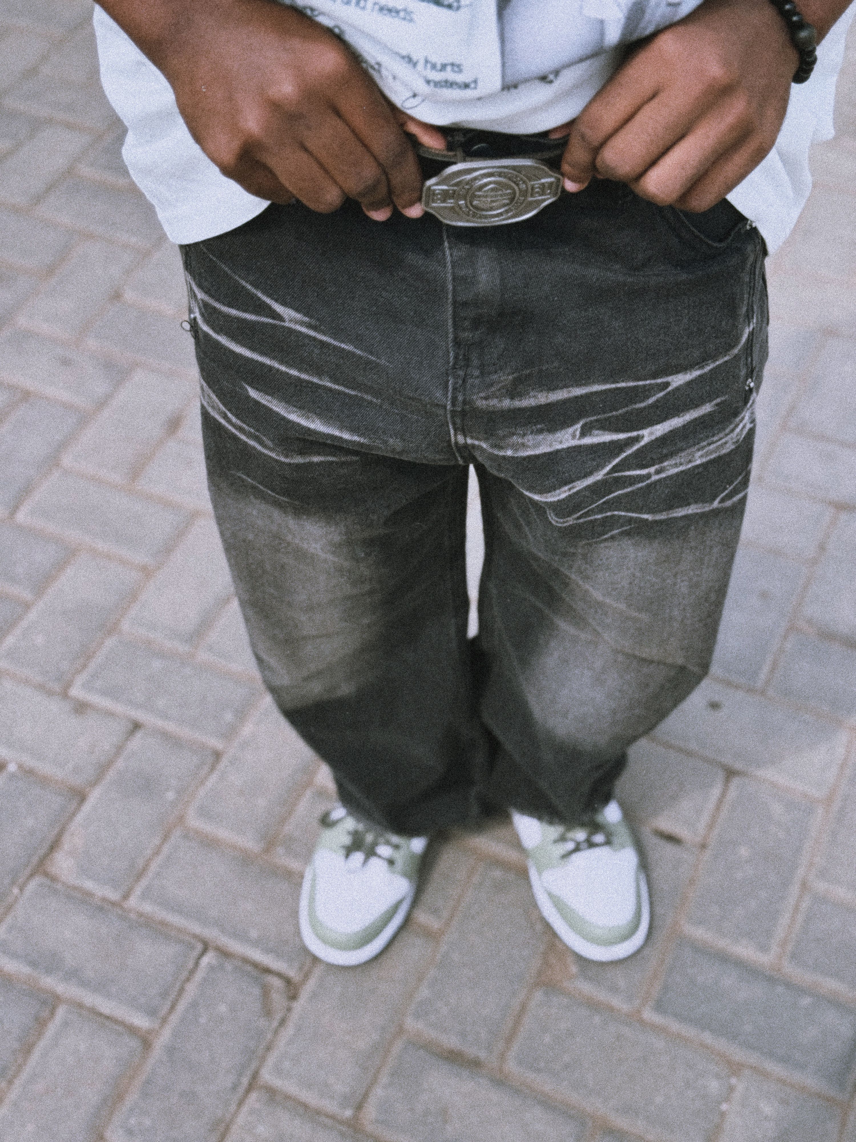 Close-up of stylish jeans and sneakers on a paved street.