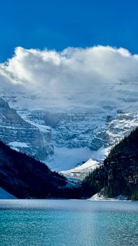 Majestic snow-covered mountains overlooking a serene blue lake under a clear sky.