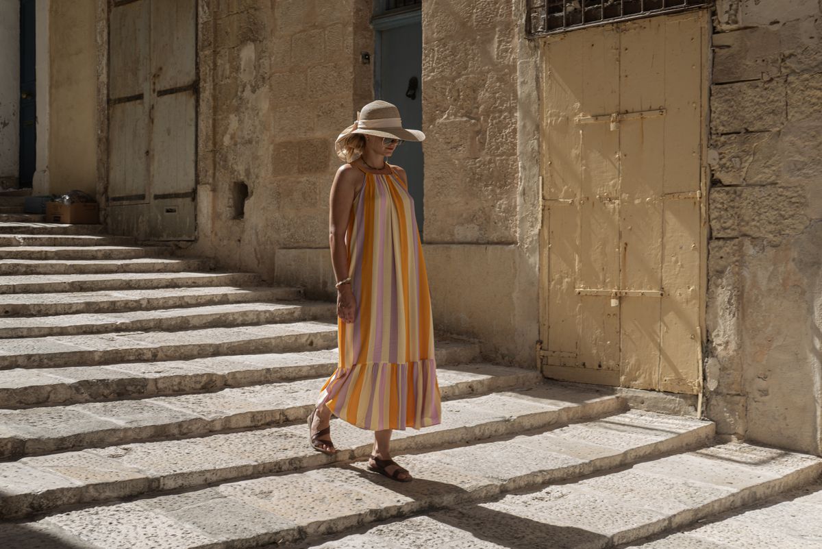 A woman in a sun hat strolling a historic European street — how to dress for a European summer