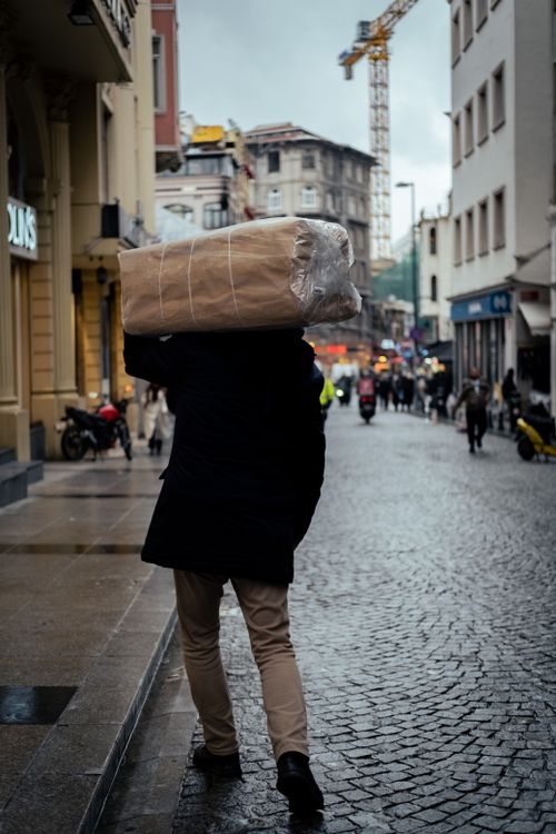 Free Man carrying large package on a cobblestone city street on a cloudy day. Stock Photo