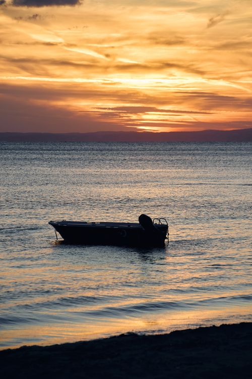 Free A tranquil boat silhouette at sunset on a serene sea, capturing a peaceful and scenic summer evening. Stock Photo