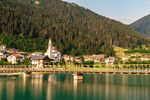 Tranquil scene featuring a bridge over Lake Misurina in Veneto, Italy with lush forests and quaint architecture in the background.