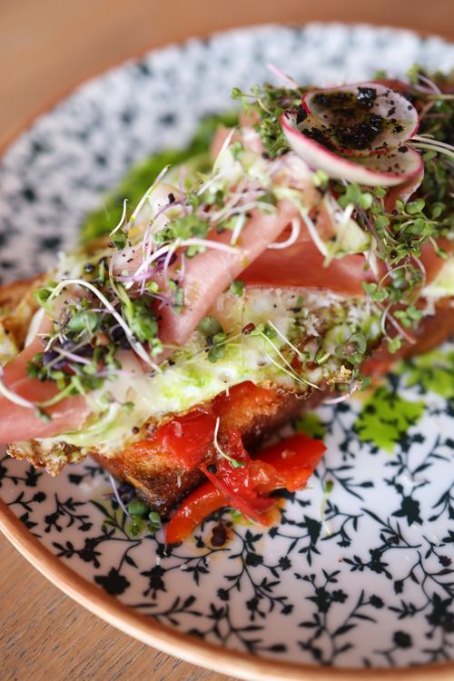 Free Delicious open-faced sandwich topped with fresh vegetables and greens on a patterned plate. Stock Photo