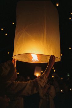 A vibrant night scene of a sky lantern festival with people releasing glowing lanterns into the night sky.