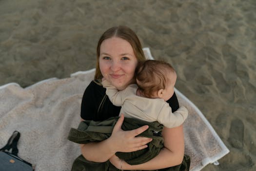 A mother lovingly holds her baby on a sandy beach in Carlsbad, CA.