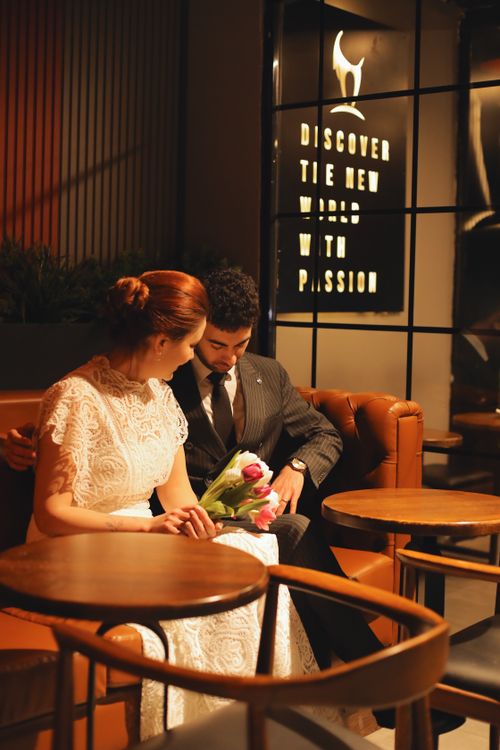 Free A couple seated in a cozy cafe with a romantic vibe, holding a bouquet of tulips. Stock Photo