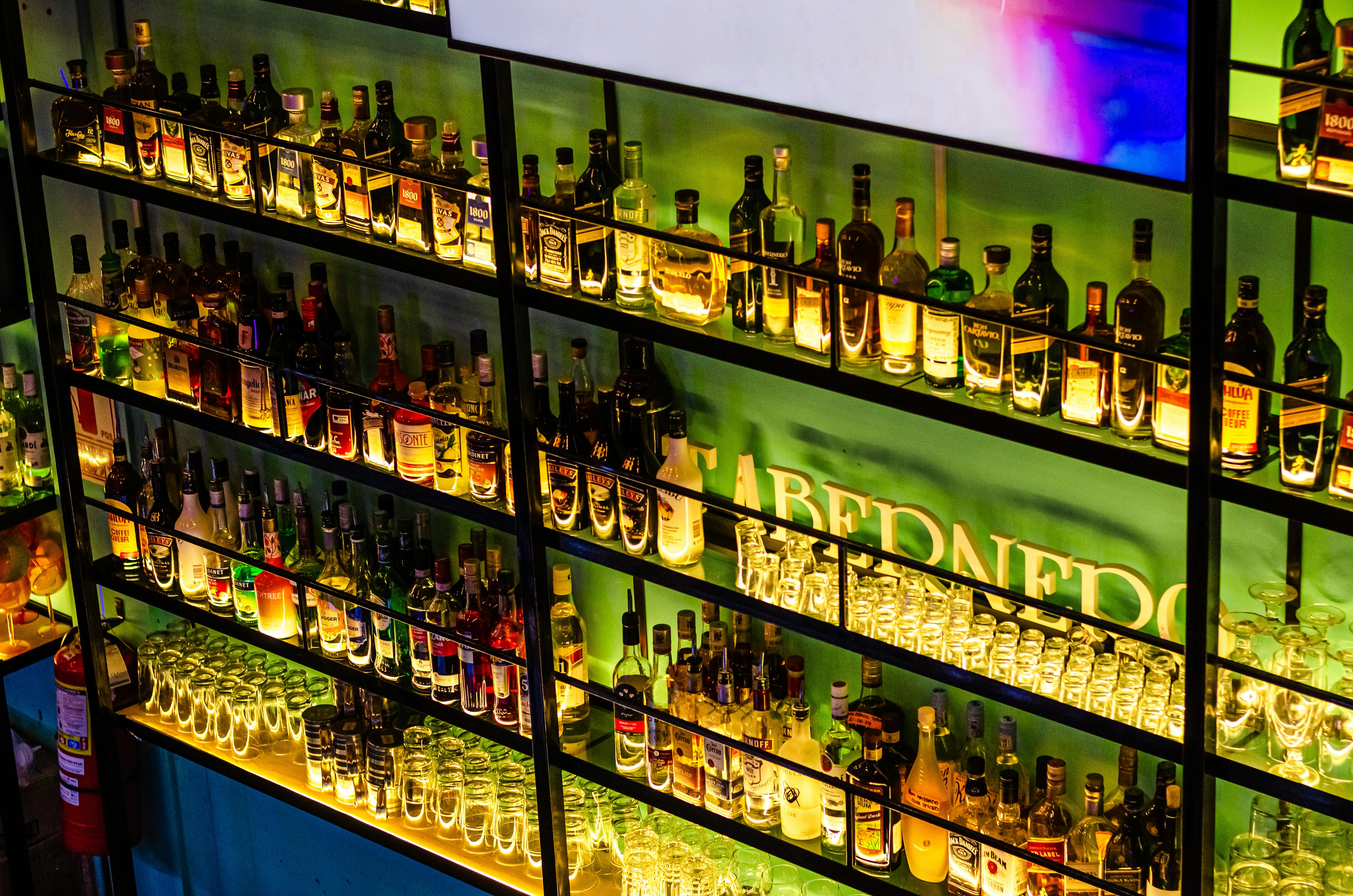 Illuminated bar shelves showcasing various liquor bottles and glasses in a vibrant setting.