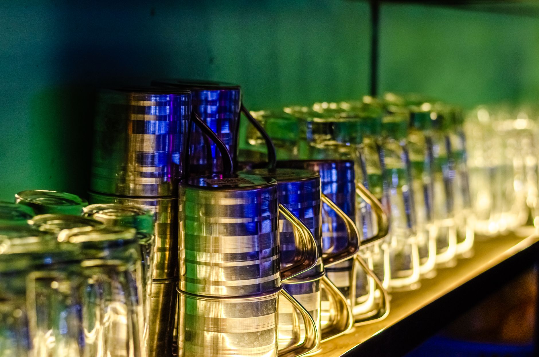 Vibrant image of a bar shelf showcasing stacked glasses and metallic pitchers with colorful lights.