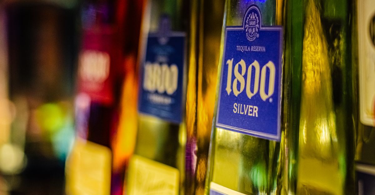 Close-up of colorful tequila bottles, highlighting 1800 Silver, in a dimly lit bar setting.