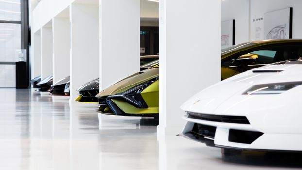 A lineup of luxury supercars in a well-lit, modern automotive museum scene.