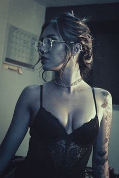 A stylish woman in lace lingerie and glasses, posing indoors with an artistic flair.
