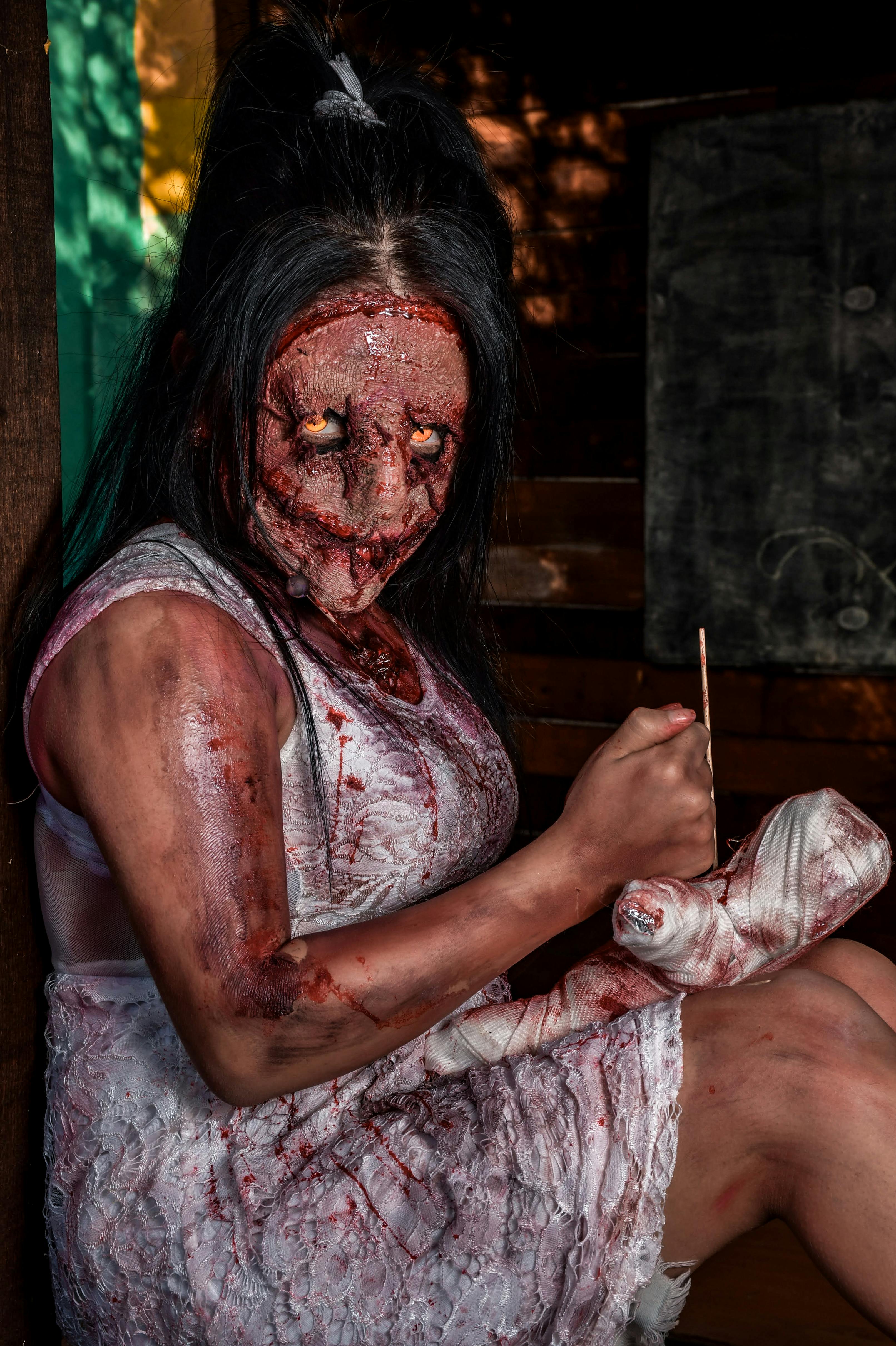 Personagem de terror assustador com maquiagem e acessórios perturbadores em um ambiente escuro.