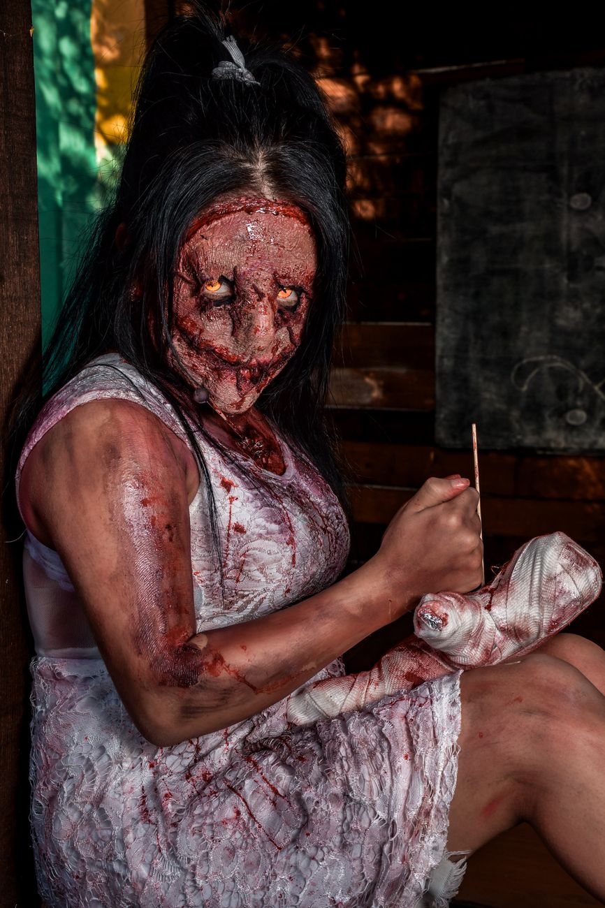 Personagem de terror assustador com maquiagem e acessórios perturbadores em um ambiente escuro.