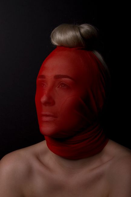 Artistic portrait with a red veil covering a woman's face, creating a dramatic visual against a black background.