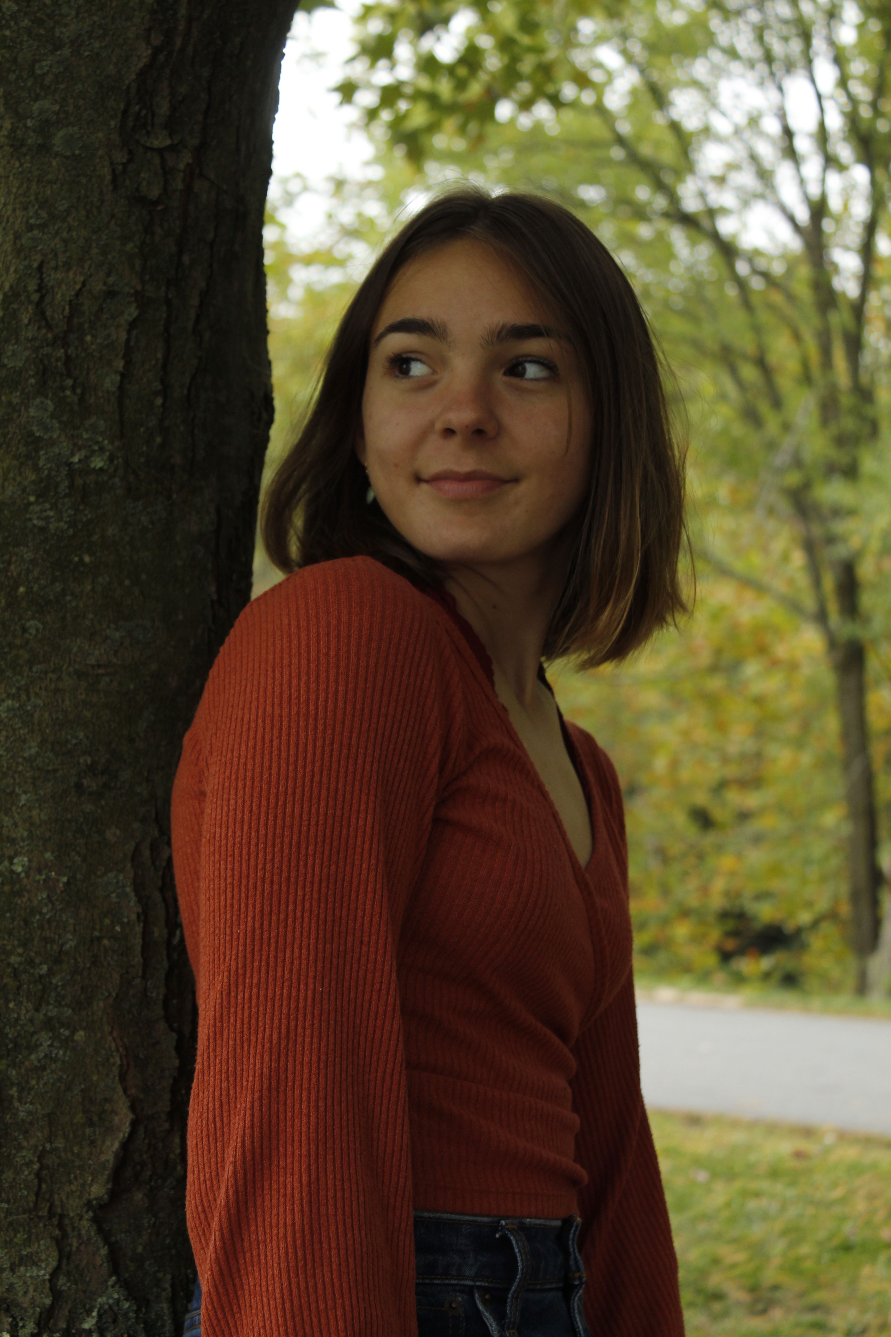 Portrait of a young woman leaning against a tree in a serene outdoor setting during fall.