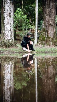 Serene scene of a woman in the forest, touching a pond, captured with reflection.