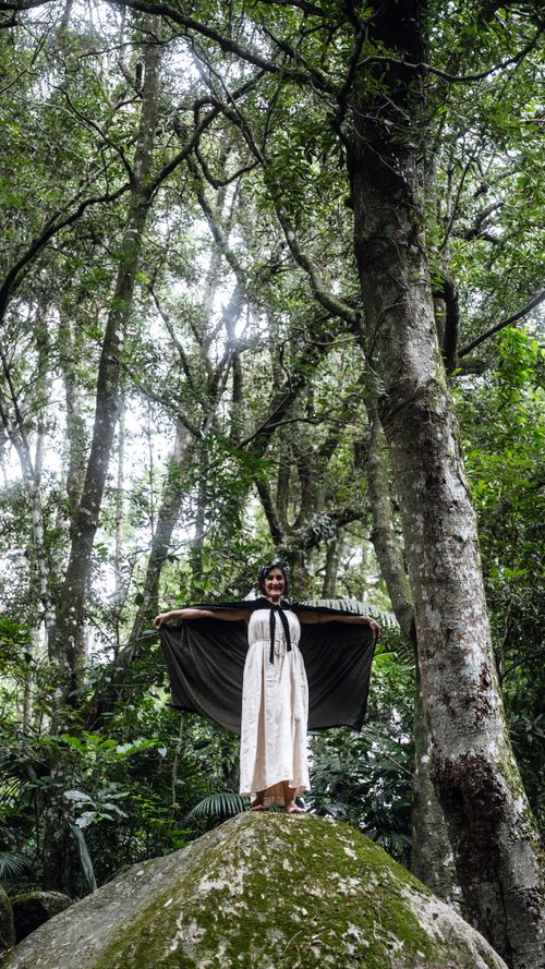 Free Woman standing on rock in a lush forest draped in a black scarf. Serene and natural. Stock Photo