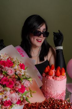Woman celebrating birthday with pink cake, flowers, and joyful expression.