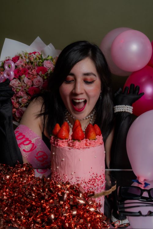 Free A woman joyfully celebrating her birthday with a pink strawberry cake and balloons. Stock Photo