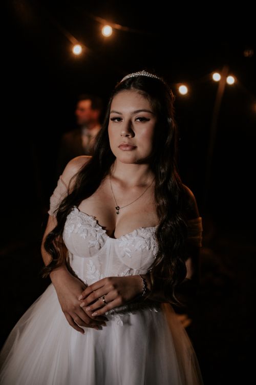 Free A graceful bride in a white gown poses at night, illuminated by string lights. Stock Photo