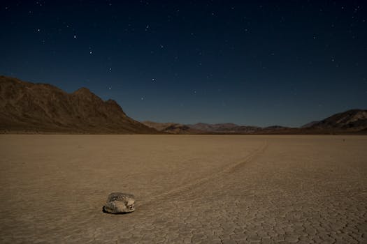 A solitary sailing stone on the vast Racetrack Playa under a starry night sky in Death Valley.
