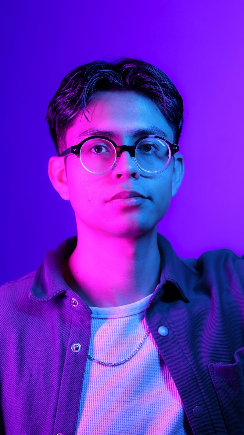 A striking neon portrait featuring a young man in glasses, highlighted by blue and purple lighting.