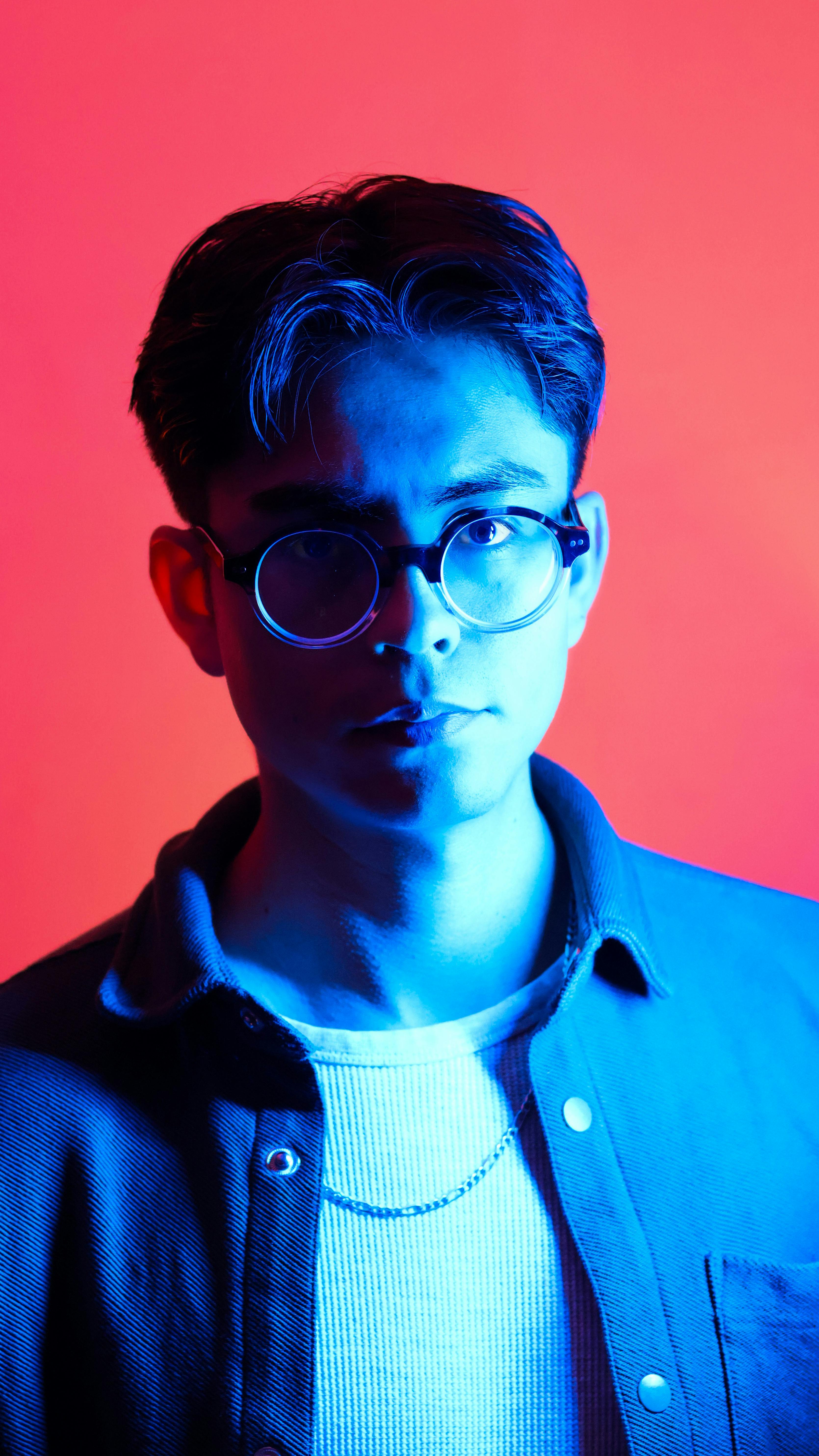 A striking portrait of a young man illuminated by contrasting blue and red lighting.