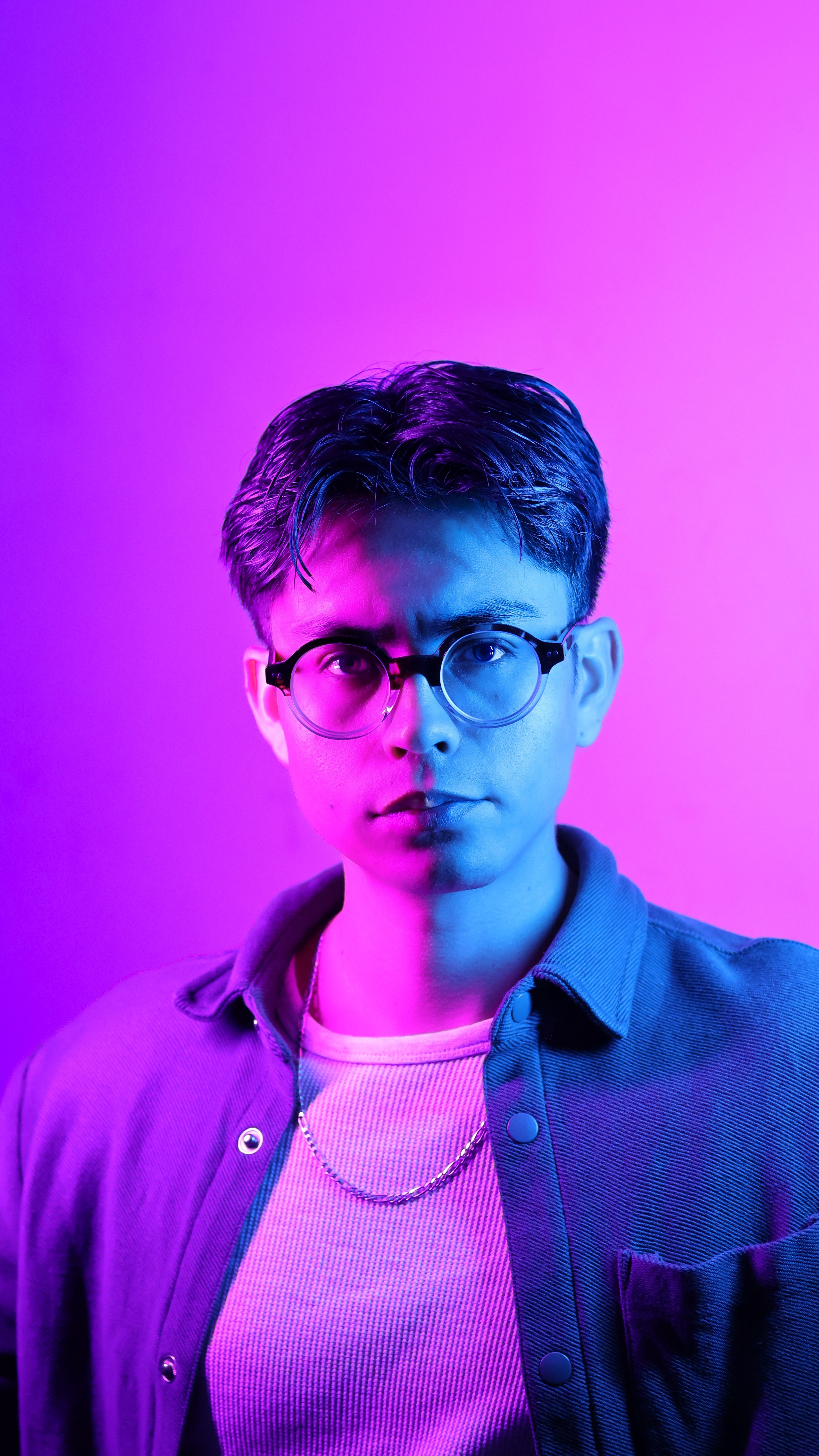 A striking portrait of a young man illuminated by blue and purple lighting, creating a dramatic effect.