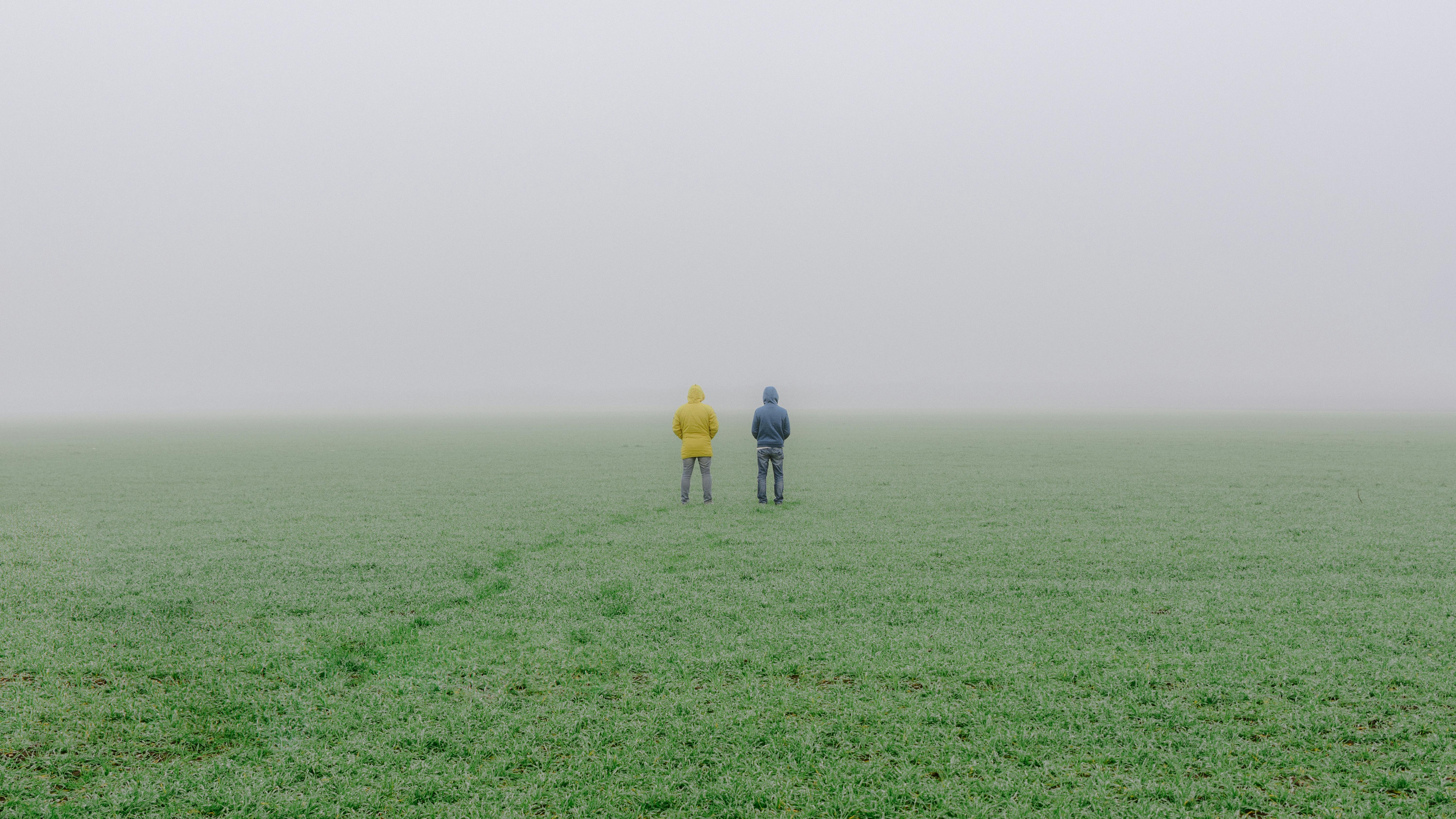 雾气弥漫的草地上站着两个穿着连帽夹克的人