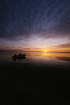 A serene sunset scene with a silhouetted boat on a calm ocean reflecting warm evening skies.