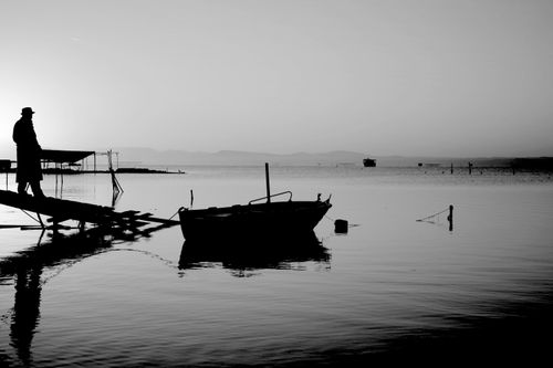 Free A lone fisherman silhouetted against a serene sunset at the lakeside, capturing peaceful solitude. Stock Photo