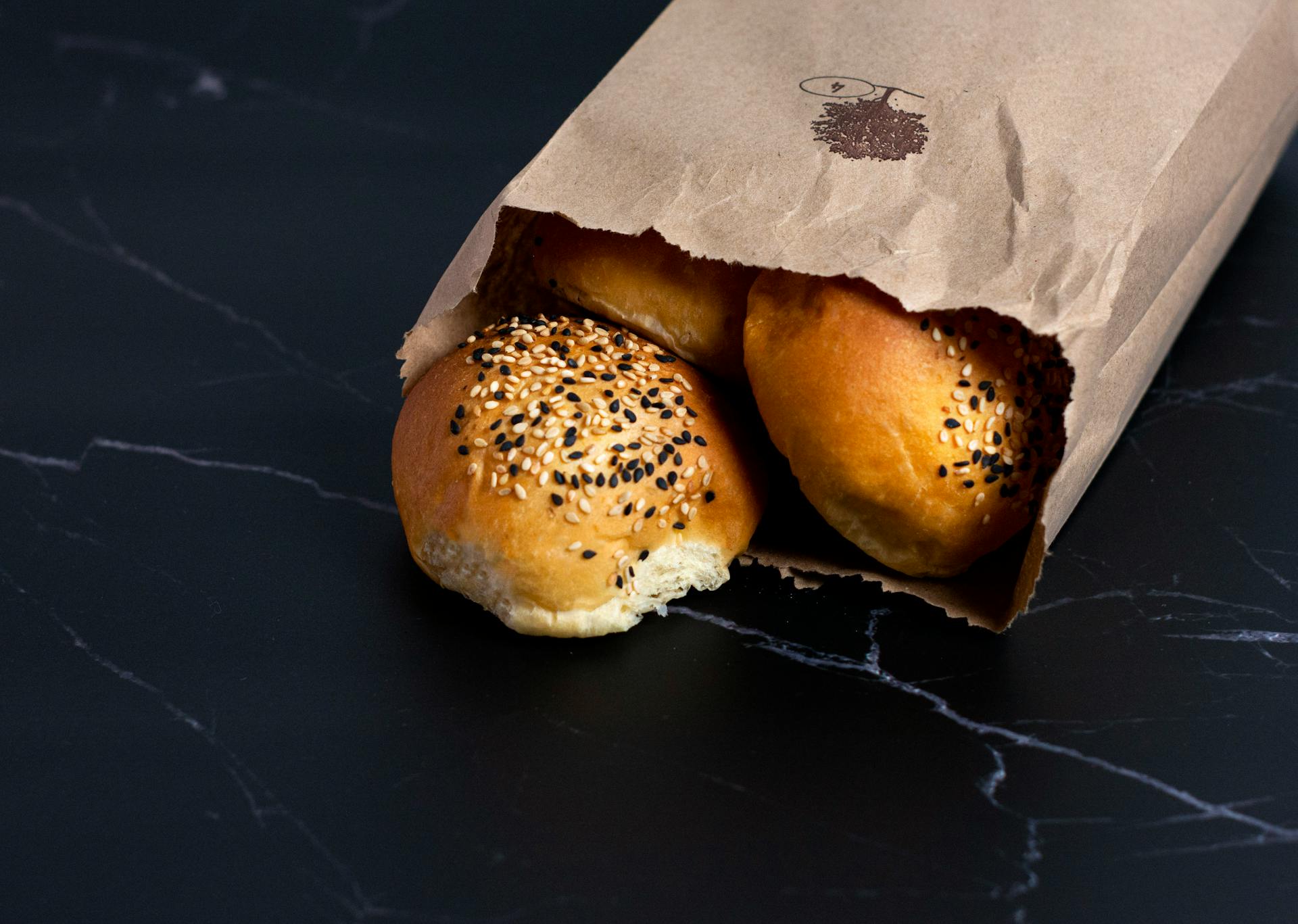 Freshly baked artisan bread with sesame seeds in a paper bag, showcasing rustic bakery quality.