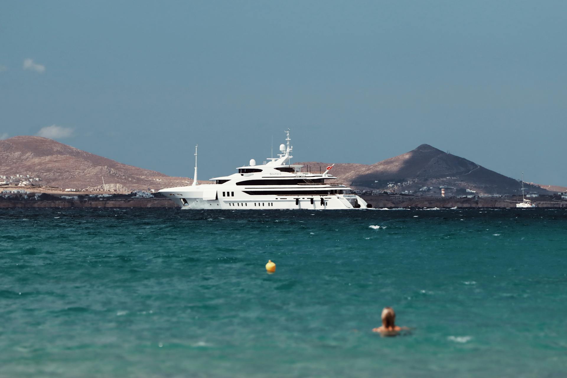 A stunning luxury yacht on the azure waters of Naxos, Greece with mountains in the background. Perfect holiday setting.