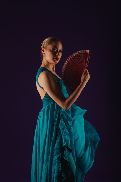 Free A woman elegantly poses in a blue dress, holding a red fan against a dark backdrop. Stock Photo