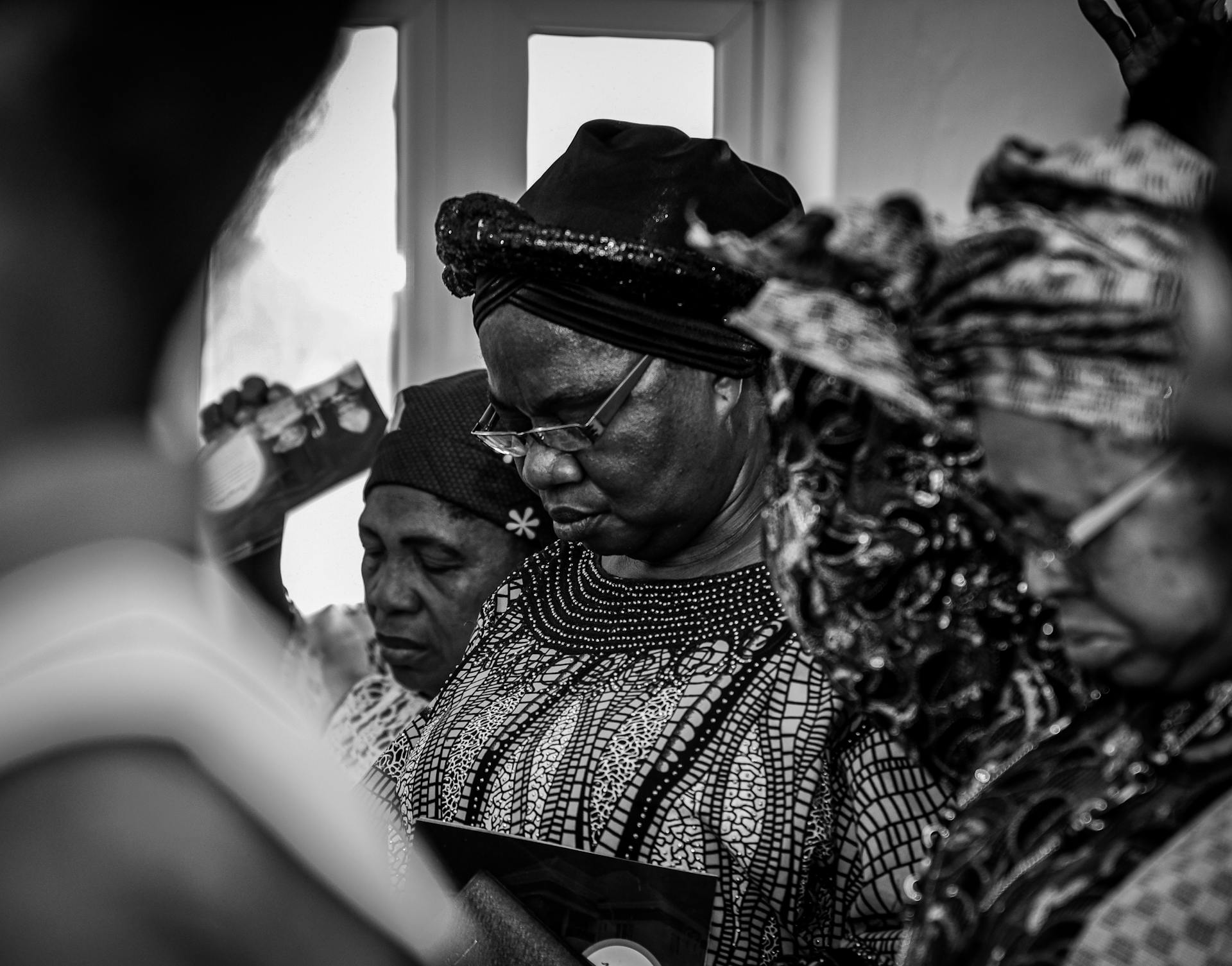 Group of African women in traditional clothing during a solemn event, captured in black and white.