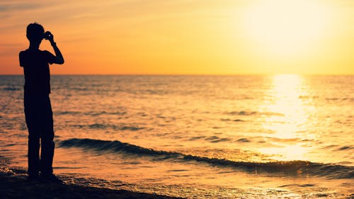 grátis Silhueta De Uma Pessoa Em Pé Na Praia Durante O Pôr Do Sol Foto profissional