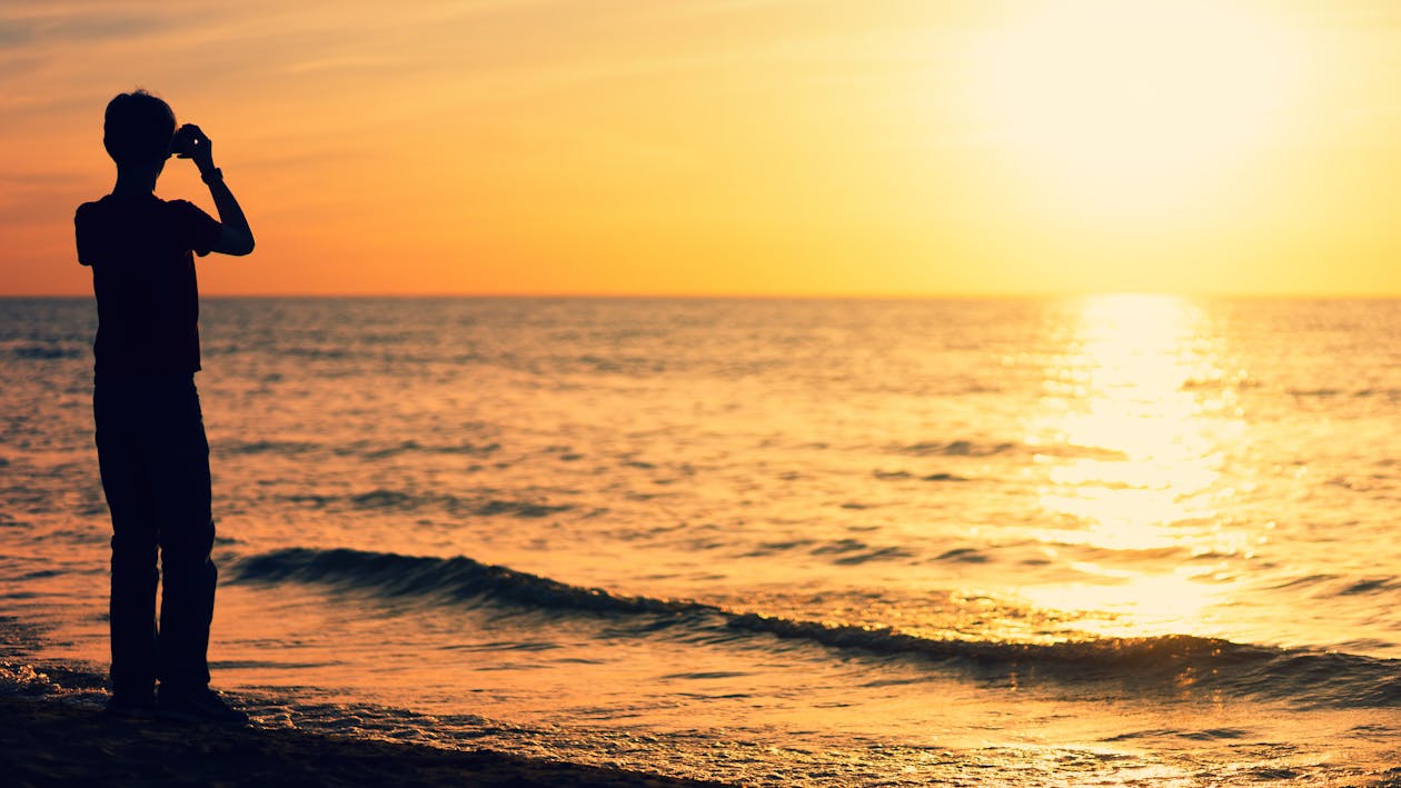 Siluet Orang Yang Berdiri Di Pantai Saat Matahari Terbenam
