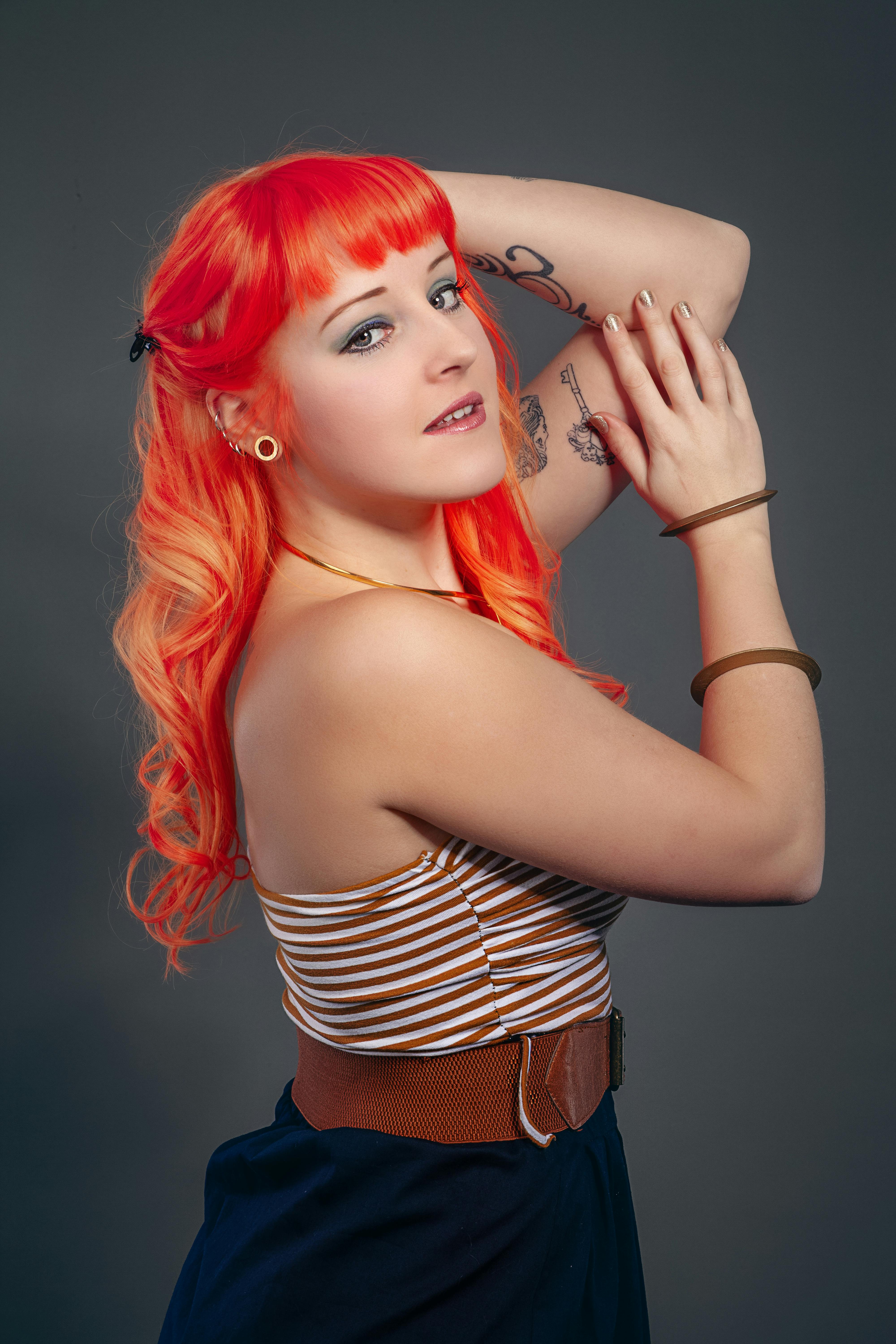 Colorful portrait of a young redheaded woman with tattoos posing in the studio.