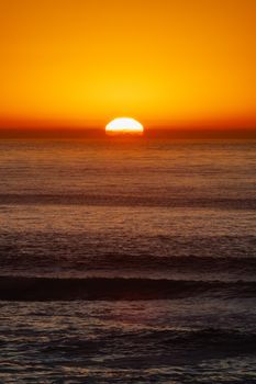 A vibrant sunset casting golden hues over the tranquil ocean horizon, creating a serene seascape.