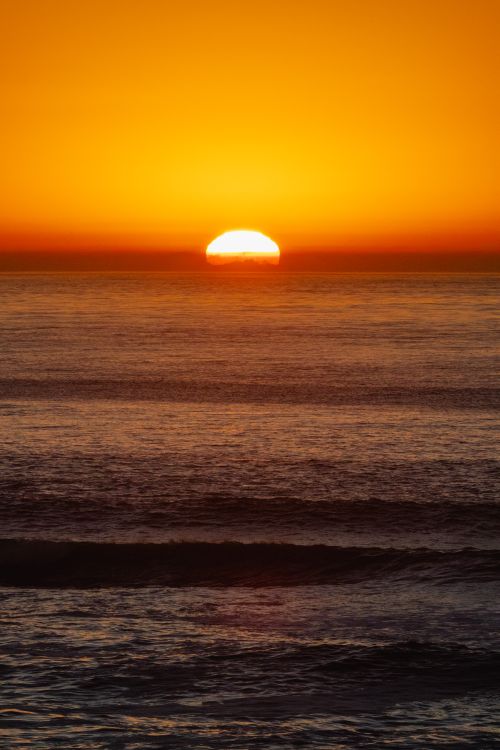 Free A vibrant sunset casting golden hues over the tranquil ocean horizon, creating a serene seascape. Stock Photo