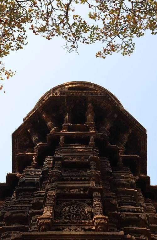 Free Low-angle view of an ancient temple with intricate carvings under a bright sky with tree branches. Stock Photo