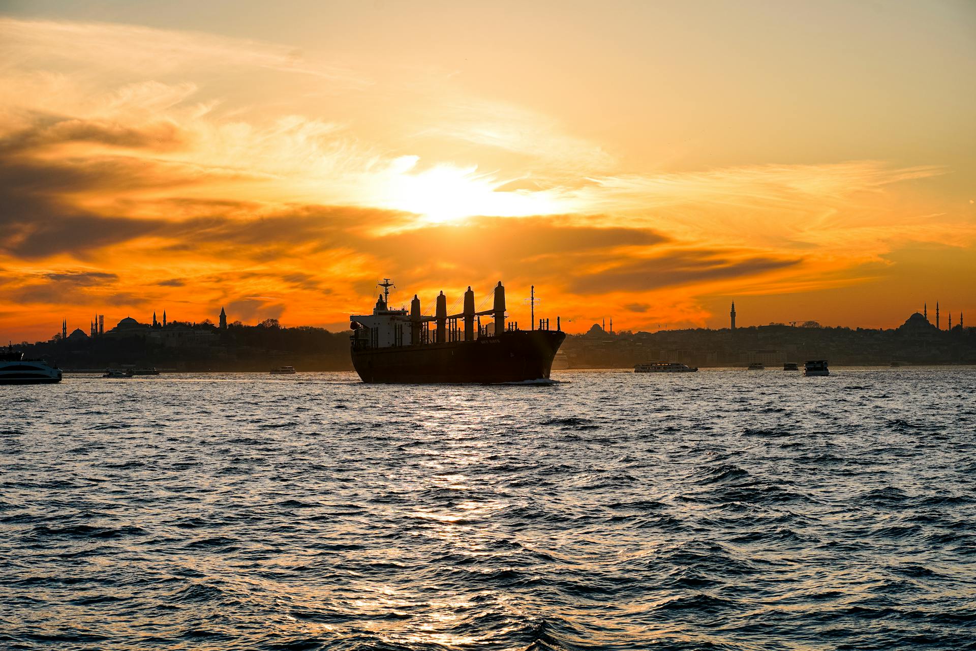 Cargo ship on Bosphorus at sunset with Istanbul's skyline creating a dramatic silhouette.