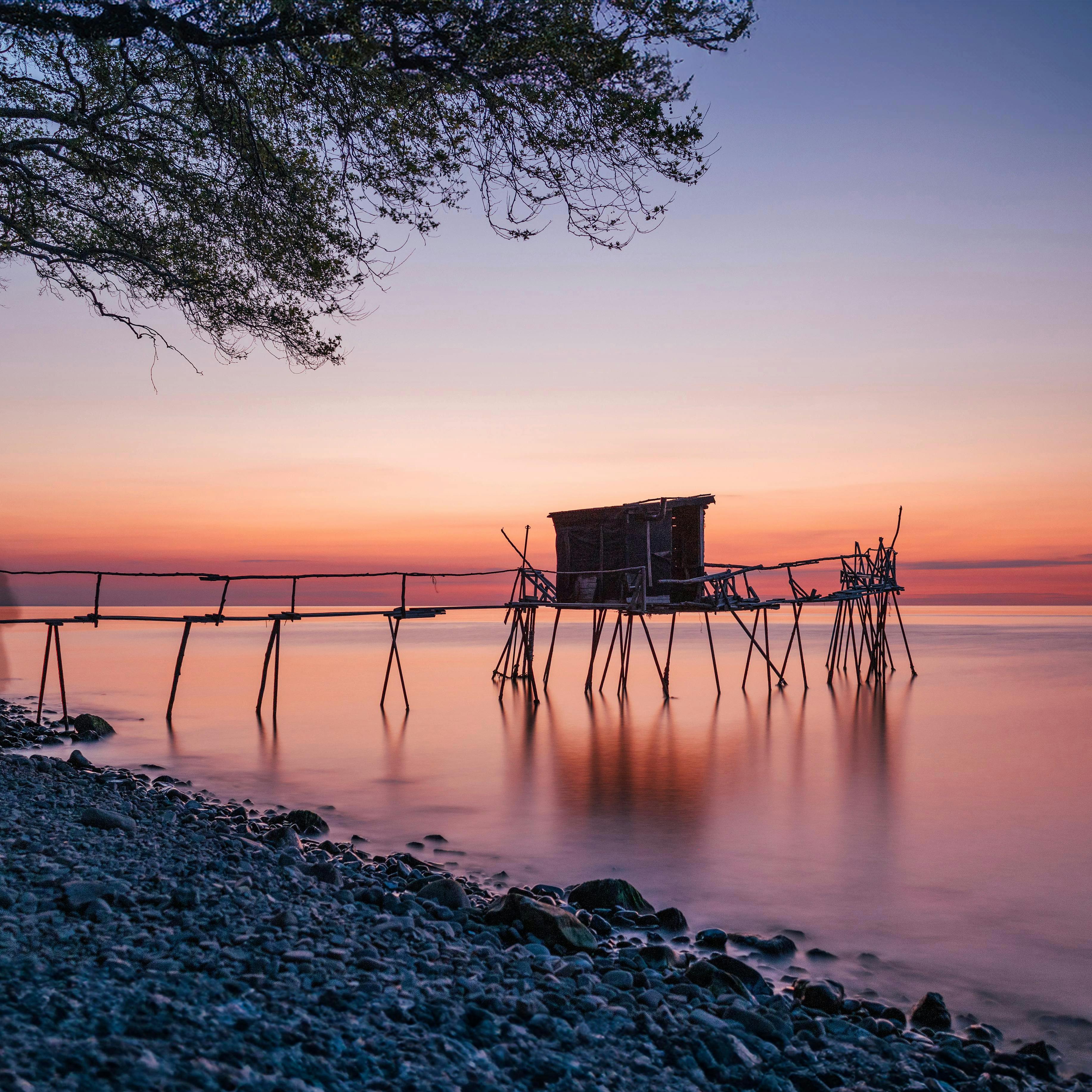 Tranquil sunrise view of a rustic fishing pier in Tekirdağ, Türkiye, with calm seas and colorful sky.