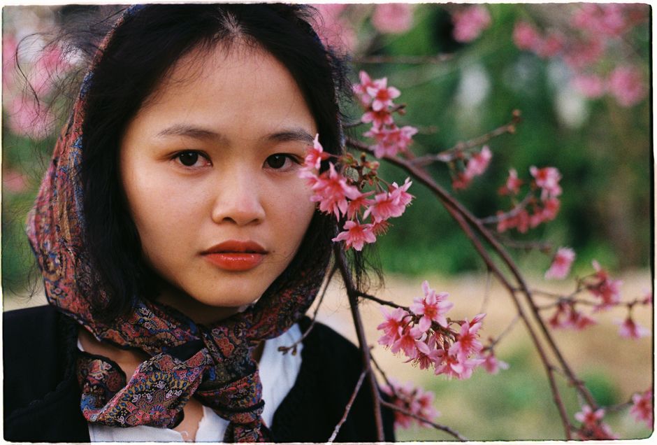 Woman in scarf among cherry blossoms, serene spring portrait.